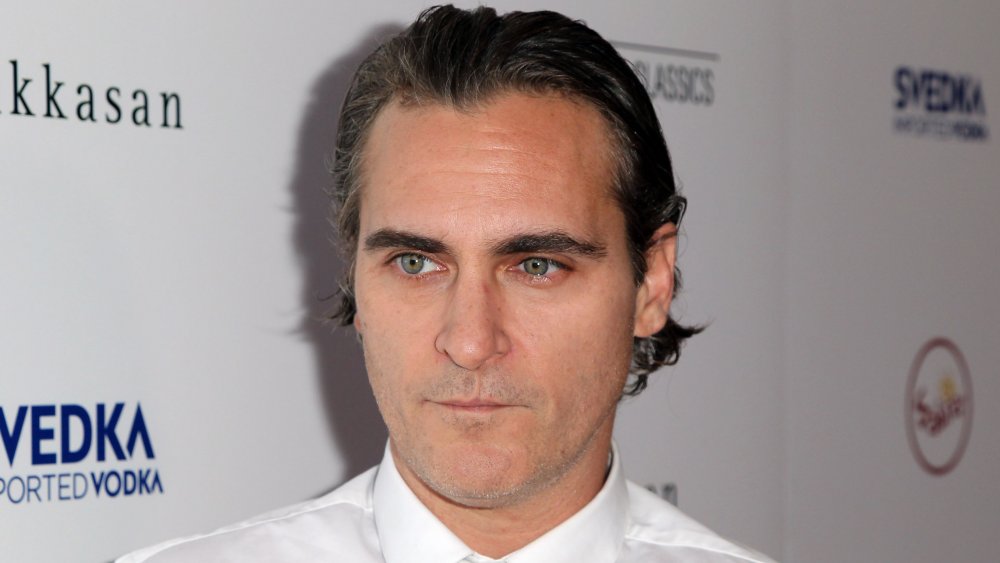 Joaquin Phoenix with slicked-back hair, in a white shirt and tie, looking serious