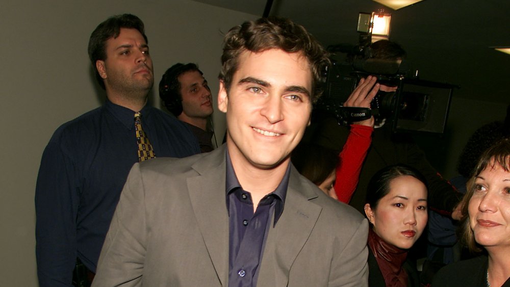 Joaquin Phoenix in a dark beige suit and blue shirt, smiling at a museum event in 2000