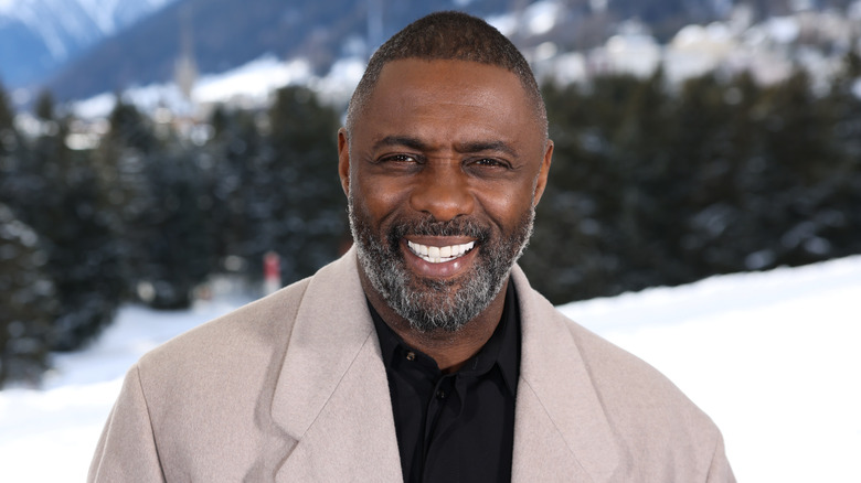 Idris Alba smiling in front of a mountain