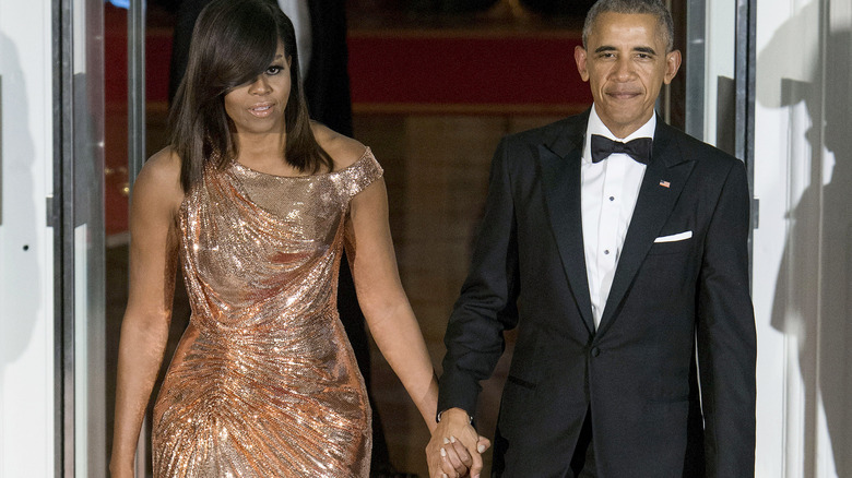 Barack and Michelle Obama hold hands at an event at the White House