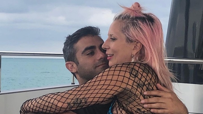 Lady Gaga wearing a mesh top sitting with Michael Polansky wearing a dark t-shirt by the water