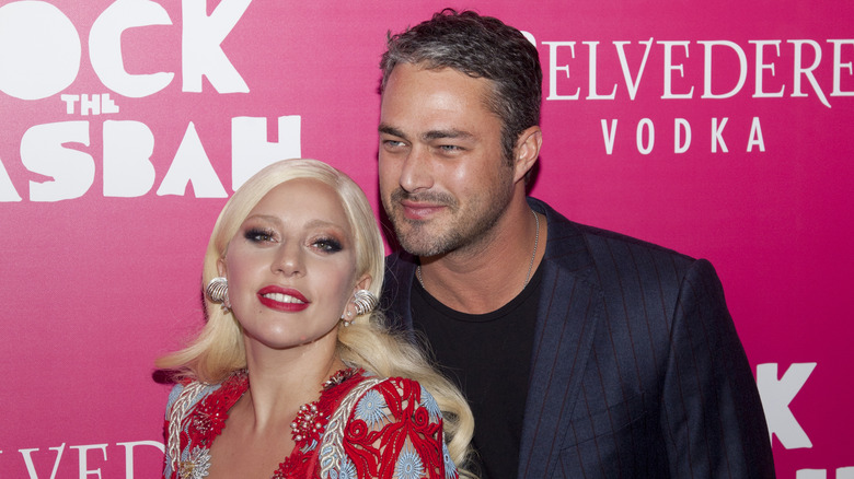 Lady Gaga wearing a multicolored beaded gown with Taylor Kinney wearing a blue pinstripe jacket on red carpet