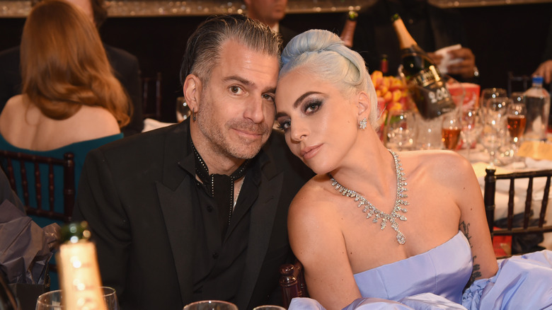 Christian Carino in a black suit and tie seated with Lady Gaga who's wearing a lavender strapless gown and diamond necklace