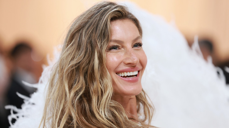 Gisele Bundchen smiling and wearing feathered dress at the 2023 Met Gala