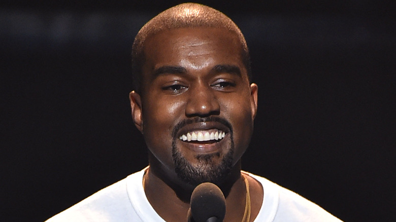 Kanye West smiling near a microphone 