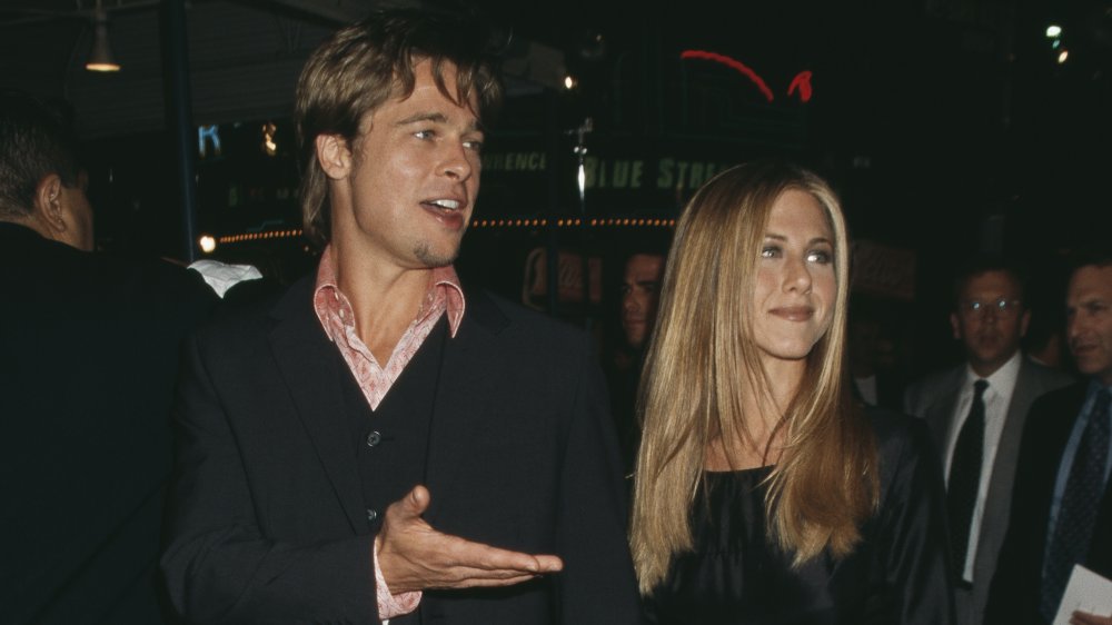 Brad Pitt and Jennifer Aniston, both wearing black, holding hands and walking a red carpet event