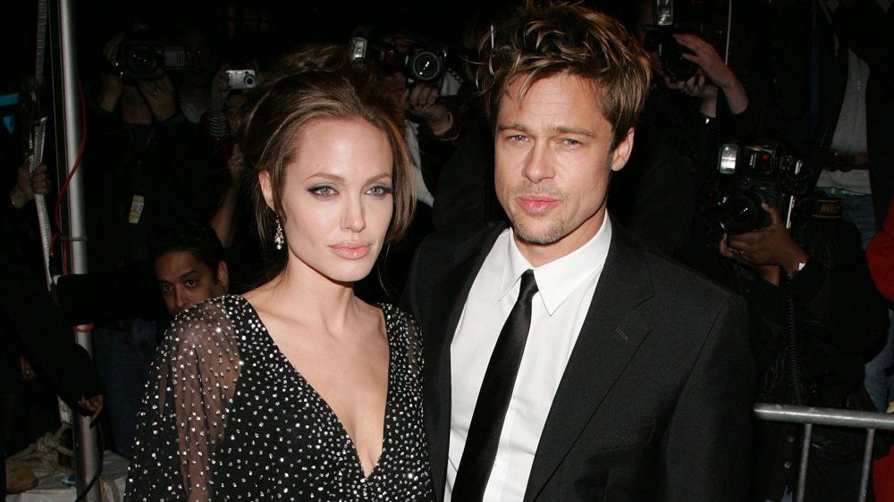 Angelina Jolie and Brad Pitt, posing together with serious expressions, surrounded by photographers
