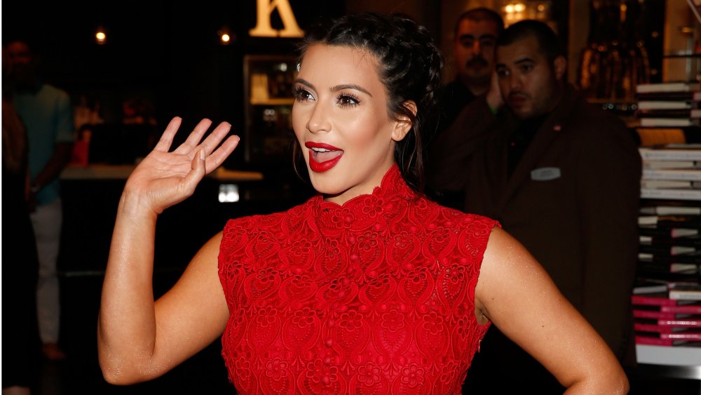 Kim Kardashian in a red dress, waving