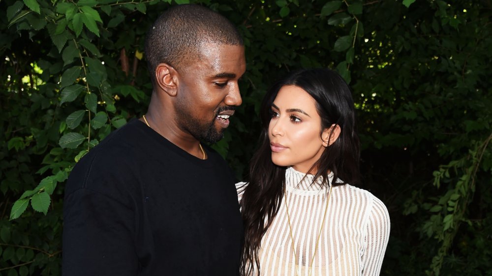 Kanye West and Kim Kardashian in front of greenery, looking at each other