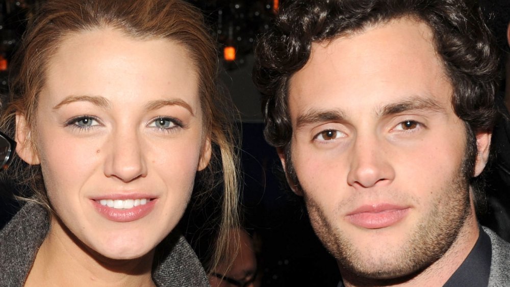 Blake Lively and Penn Badgley, both wearing grey outfits with small smiles