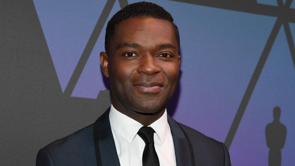 David Oyelowo in a dark blue, black-lined suit, posing with a small smile at the Oscars