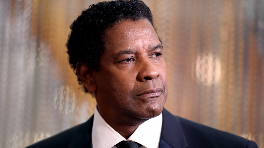 Denzel Washington in a classic black suit and tie combo, looking serious while gazing off to the side