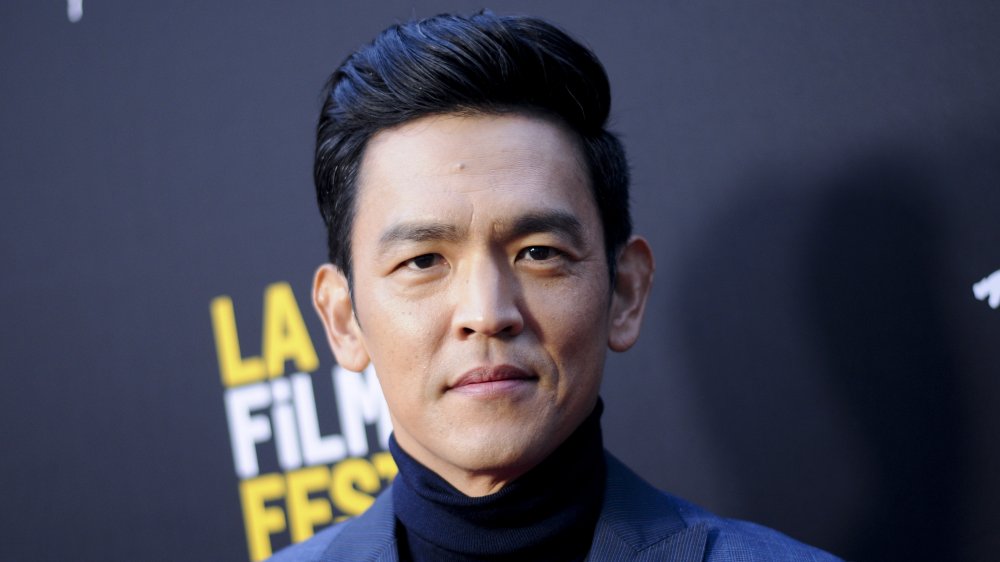 John Cho in a blue blazer and turtleneck, posing with a serious expression