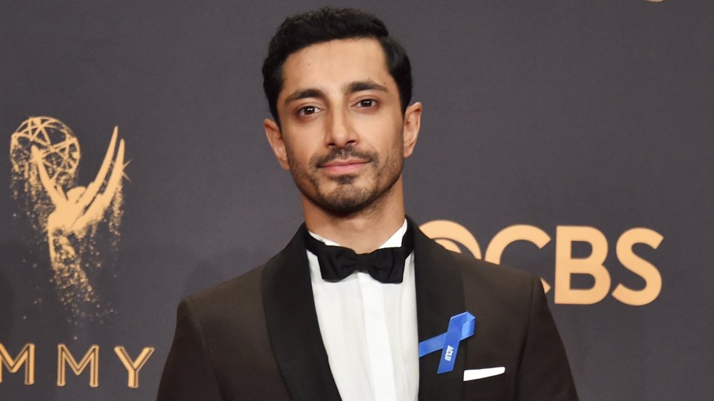 Riz Ahmed in a black suit and bow tie, posing with his Emmy