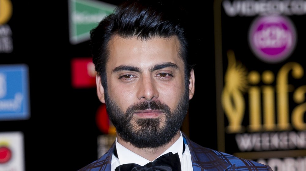 Fawad Khan in a blue-plaid suit jacket and black bow tie, posing with a neutral expression