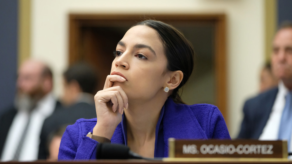 Alexandria Ocasio-Cortez listening while leaning her chin on her hand