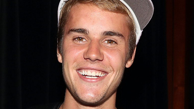 Justin Bieber smiling in a white baseball cap