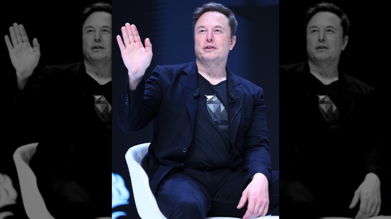 Elon Musk with his hand raised