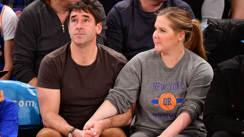 Chris Fischer and Amy Schumer holding hands at a basketball game