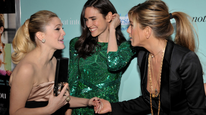 Jennifer Aniston and Drew Barrymore shaking hands in front of Jennifer Connelly