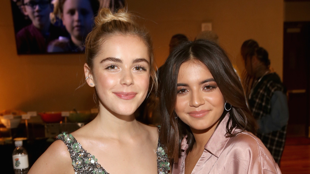 Kiernan Shipka, blond hair up in bun, smiling; Isabela Merced, smiling, hair down, at a party