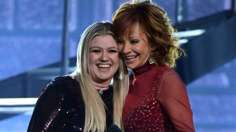 Kelly Clarkson smiles on stage with Reba McEntire