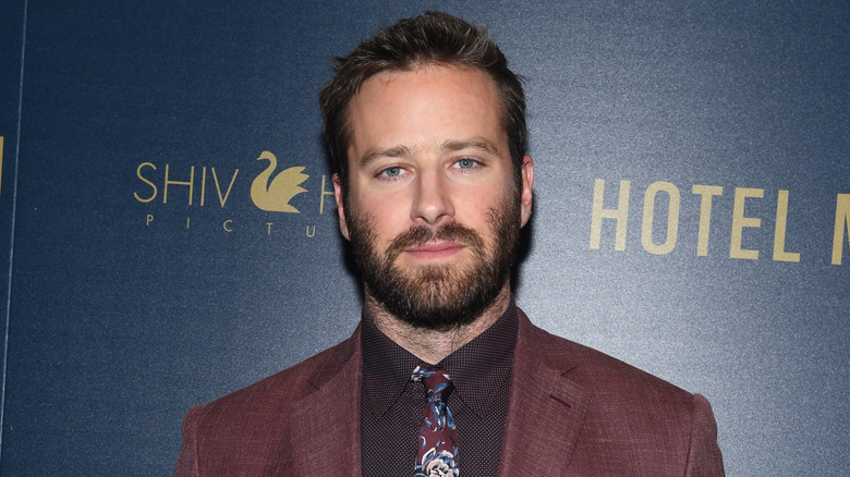 Armie Hammer wearing a maroon jacket and black patterned shirt with a paisley tie