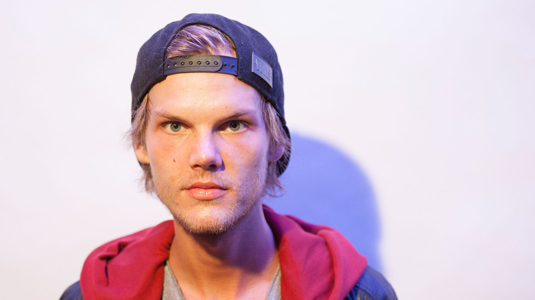 Avicii poses in a hoodie and cap.