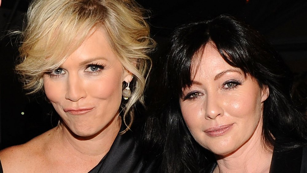 Jennie Garth and Shannen Doherty, both with small smiles and wearing black at an industry event