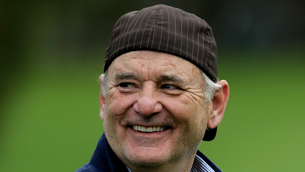 Bill Murray wearing a cap backwards as he grins at something