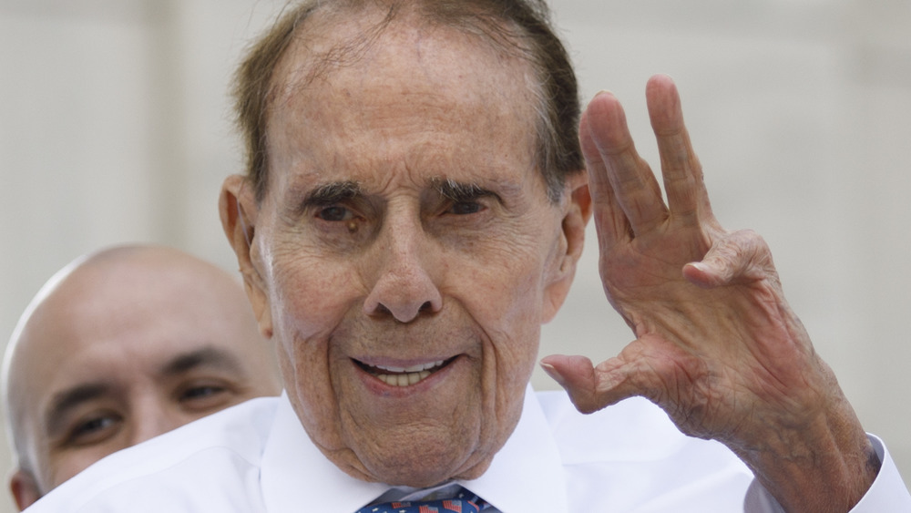 Bob Dole, smiling, waving, in a collared shirt and tie