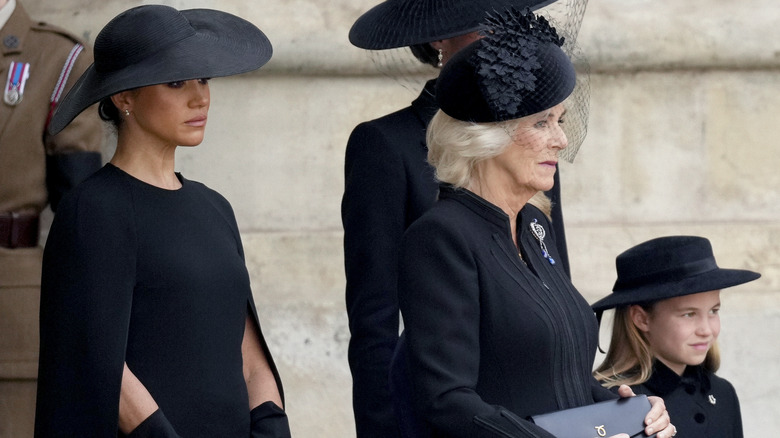 Camilla holding purse, with Meghan Markle and Princess Charlotte