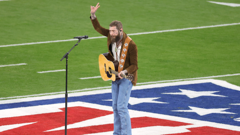 Post Malone giving peace sign while playing guitar on football field