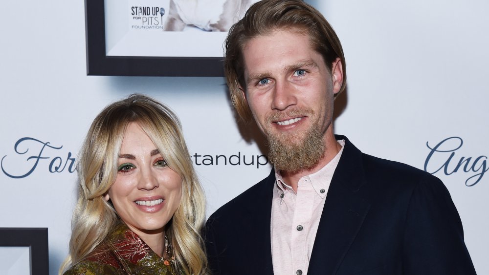 Kaley Cuoco and Karl Cook in front of a promotional wall, smiling