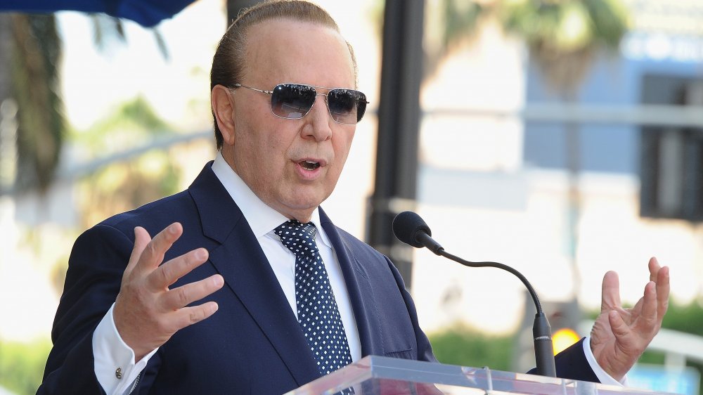 Tommy Mottola speaking at a podium, sunglasses on