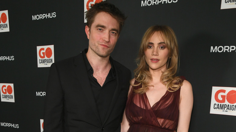 Suki Waterhouse and Robert Pattinson stand at red carpet event