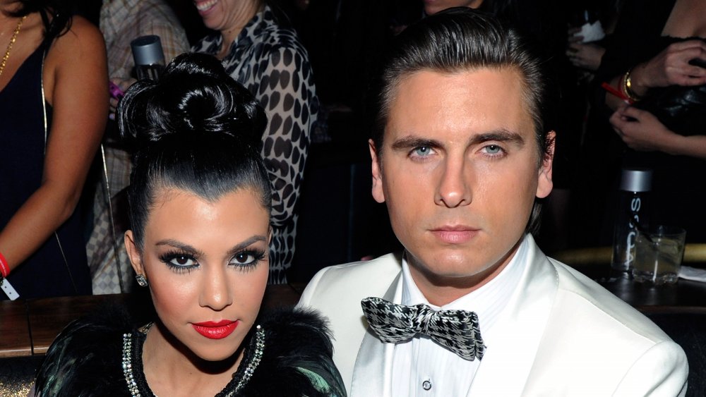 Kourtney Kardashian with red lips and high bun, next to Scott Disick