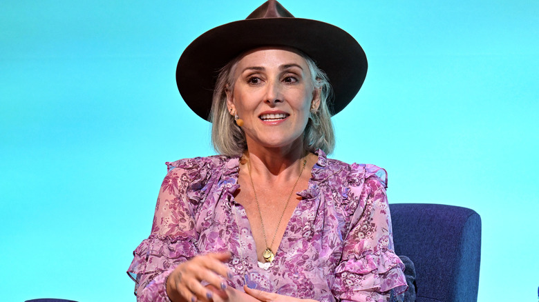 Ricki Lake wearing a purple floral dress and brown hat