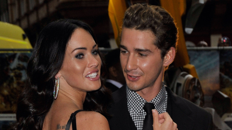 Shia LaBeouf looking at Megan Fox as she poses on a red carpet