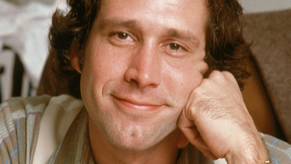 Chevy Chase smiling, resting his face on his fist 