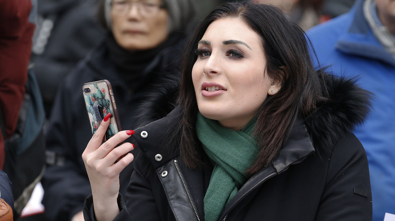 Laura Loomer in a crowd wearing a jacket and holding a phone