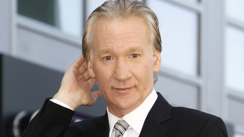 Bill Maher with his hand behind his head, looking on