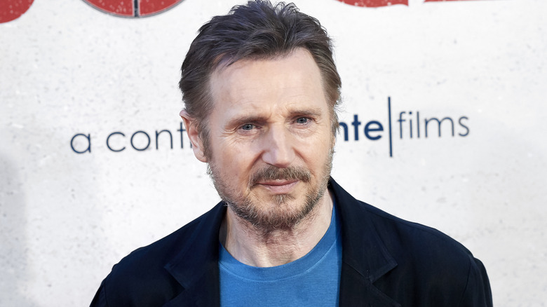 Liam Neeson posing with a neutral expression in a blue outfit