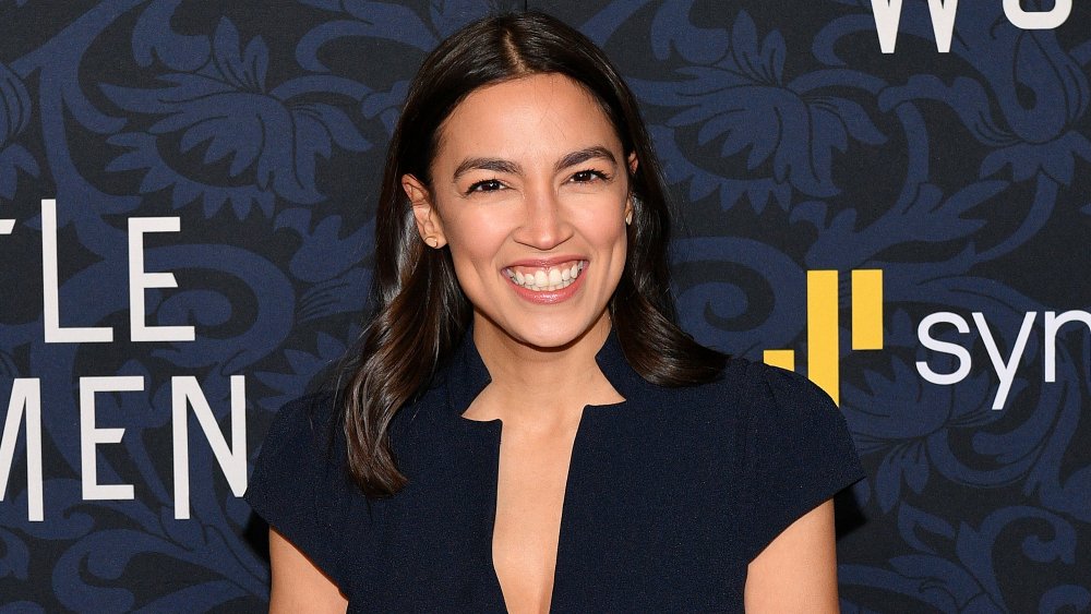 Alexandria Ocasio-Cortez wearing a navy blue dress, smiling big