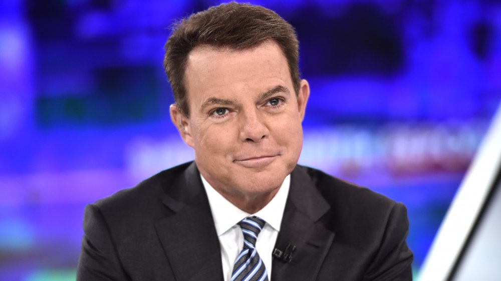 Shep Smith in a black suit, white shirt, and blue-striped tie, with a small smile on his show