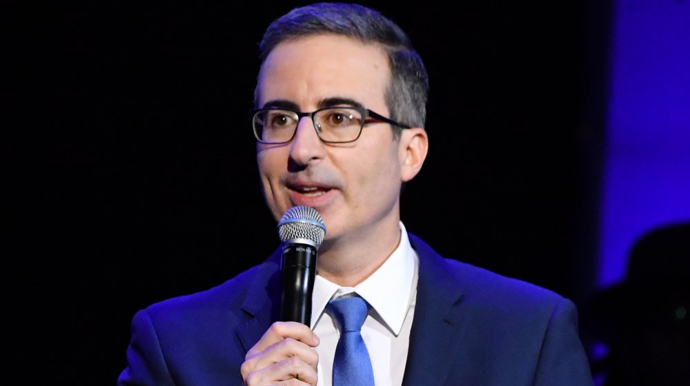 John Oliver wearing a blue suit, performing stand-up