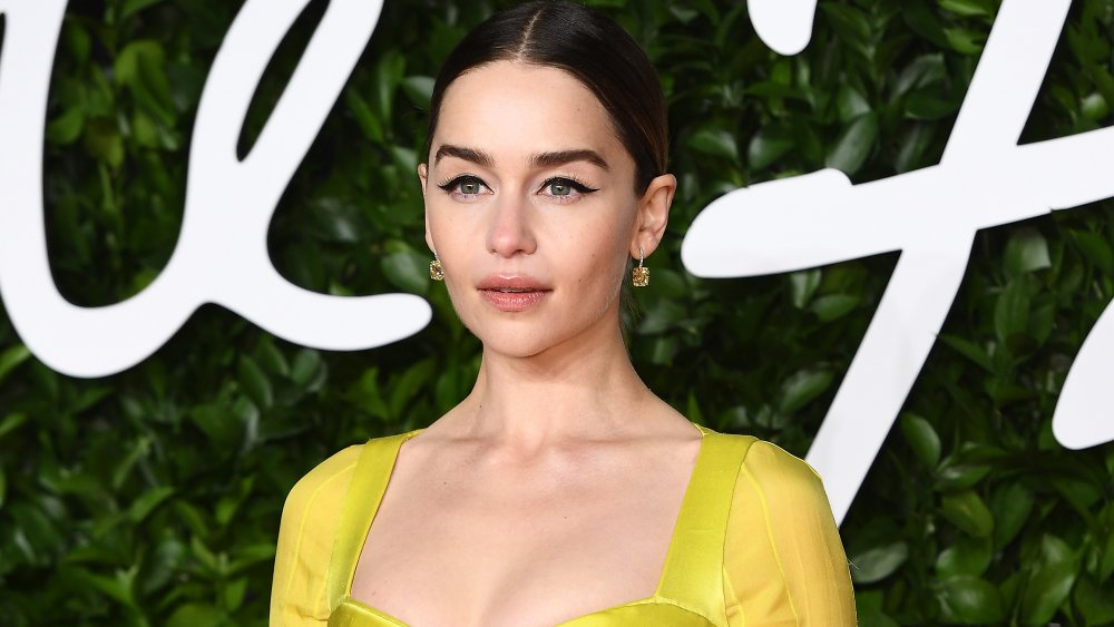 Emilia Clarke with hair slicked back in yellow dress