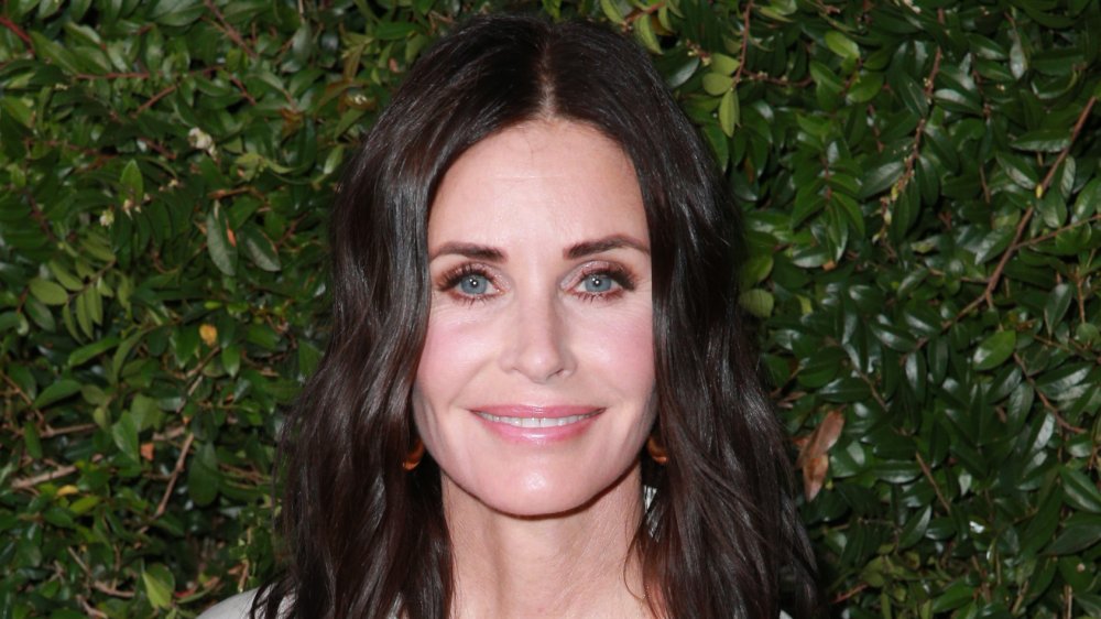 Courteney Cox in a white-and-black dress, smiling at an outdoor event