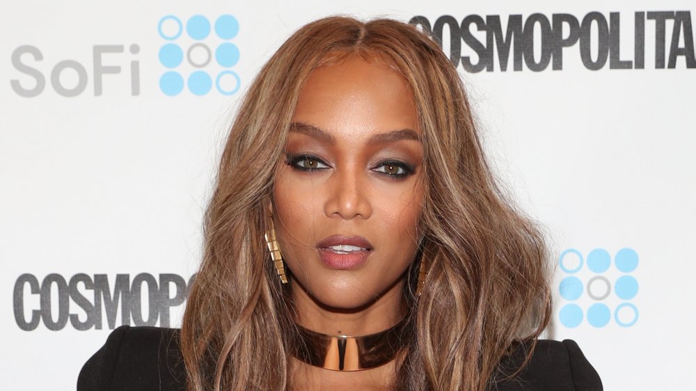 Tyra Banks in a black dress, posing on the red carpet with a neutral expression