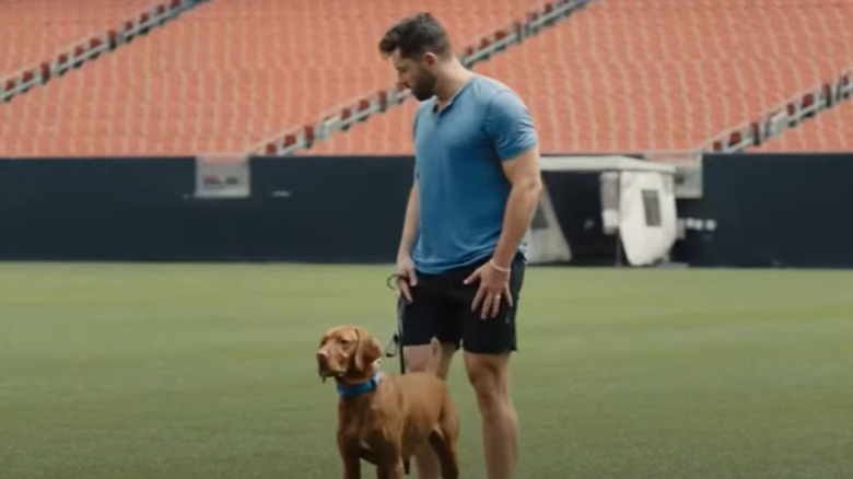 Baker Mayfield standing on football field with dog